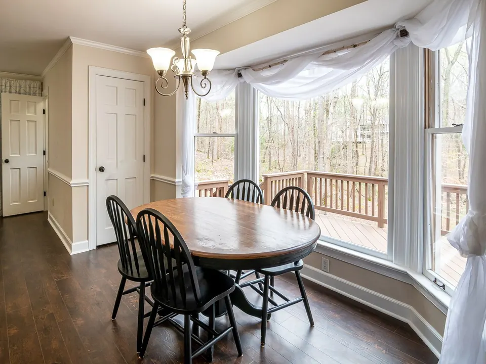 Dining room with a white bay window overlooking a wooded backyard
